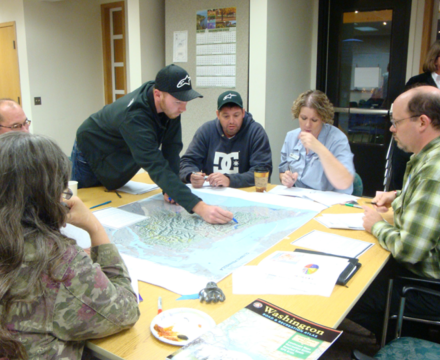 A group of people leaning over a map and pointing at different areas