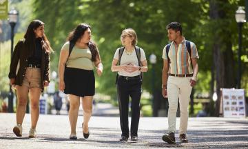 President Ann Cudd walking with three students in the park blocks wearing a backpack. 