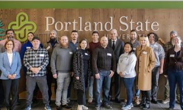 Veterans pose in front of the Portland State sign from 2023 visit by U.S. Secretary of Veterans Affairs ​​Denis R. McDonough