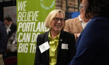 President Ann Cudd talking with someone in front of a sign that says "We Believe Portland Can Do Big Things"