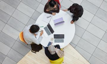 Students sitting around a table with some laptops, photographed from above. 