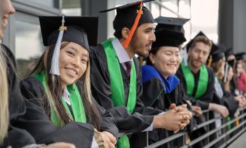 Students in commencement regalia stand smiling in a row. 