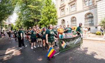 People in PSU shirts participating in a Pride Parade behind a PSU banner with Rainbow detailing.