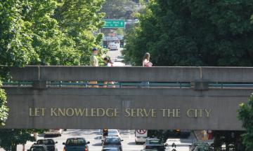 Let Knowledge Serve the City on the skybridge with people walking across it and trees in the background.