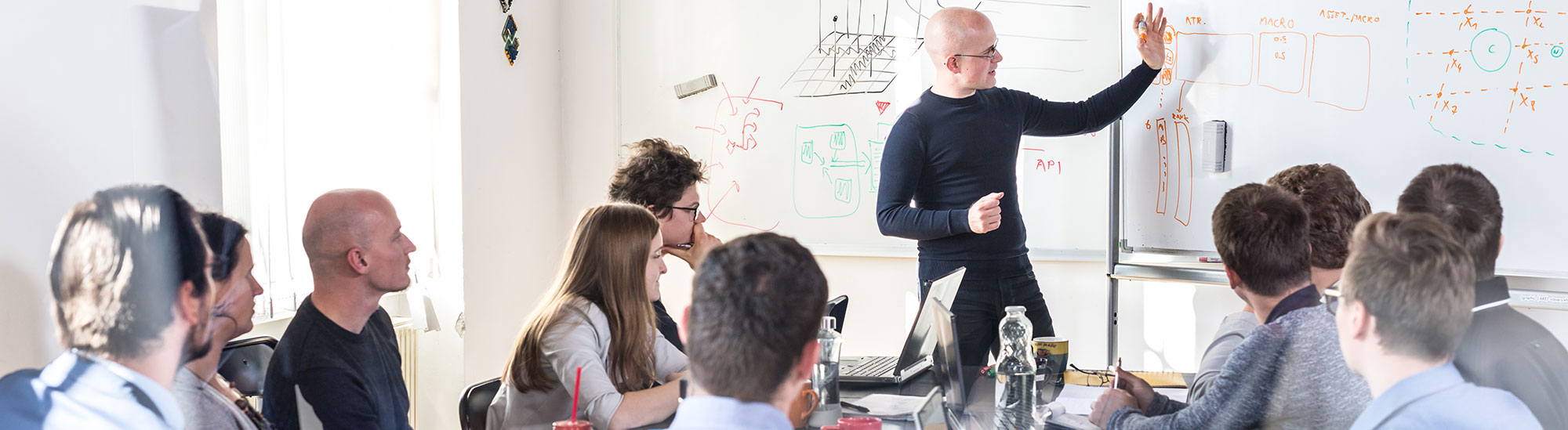 Man at white board in front of class explaining something