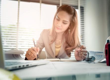 A person who is writing on paper with a laptop in front of them.