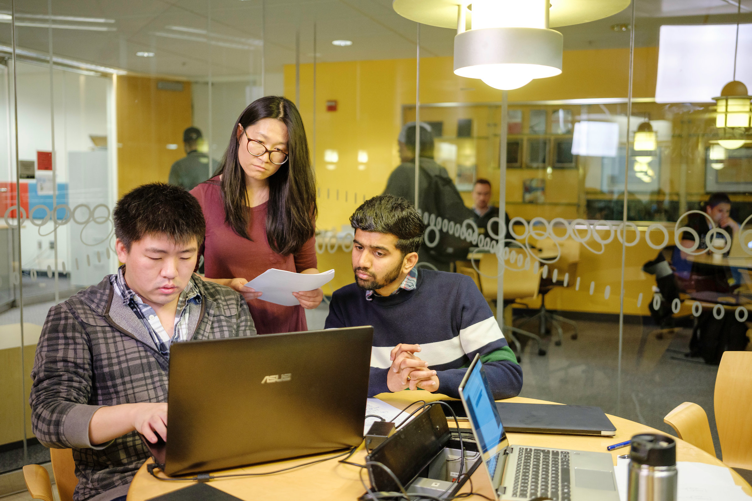 Three students around table looking at laptops