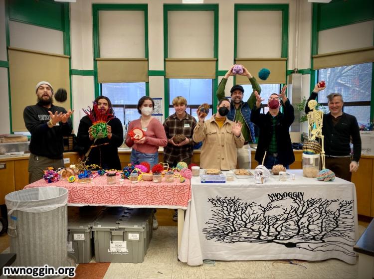 NW Noggin volunteers stand behind a table, holding various neuroscience models