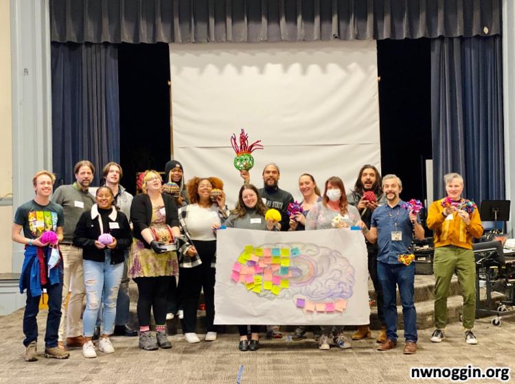 A group of NW Noggin volunteers hold neuroscience models and a banner with the parts of the brain labeled