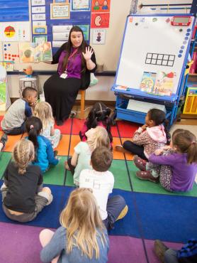 Elementary school teacher reading a book to kids seated on carpet