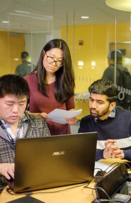 Three students around table looking at laptops