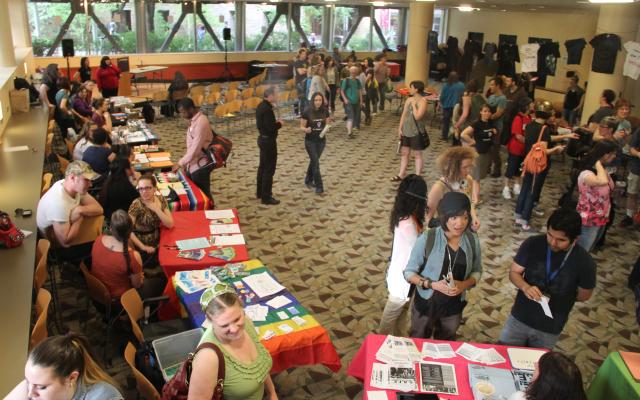 many people move through take back the night in the smith building. There are several tables with organization representatives and many people chatting