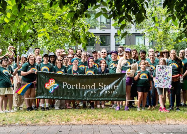 Large group of smiling people holding rainbow PSU logo banner