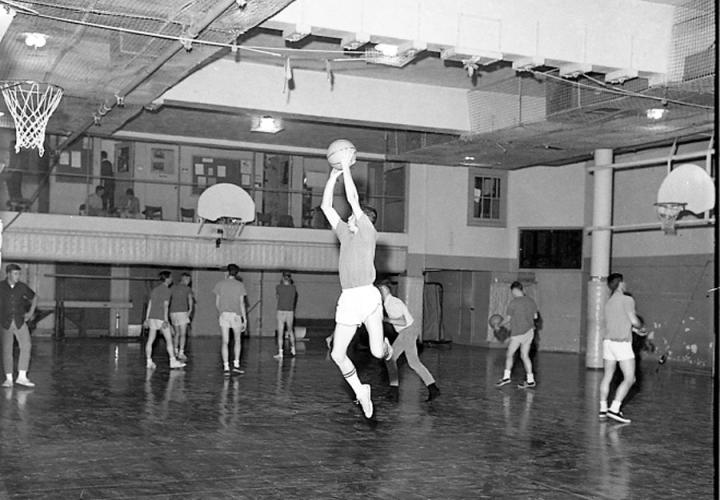 A group of students in a gym playing basketball. 