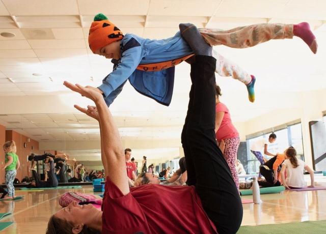 A parent holds their child up in a family-friendly yoga class