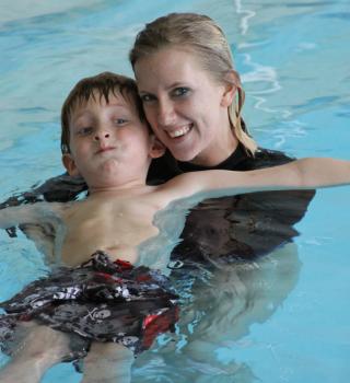 A woman smiles while swimming with a youth member in the Rec Center pool