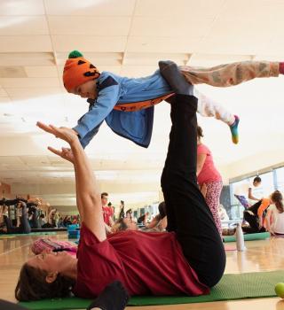 A parent holds their child up in a family-friendly yoga class