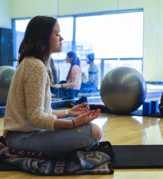 Person meditating; sitting cross legged with eyes closed and palms up towards the sky.