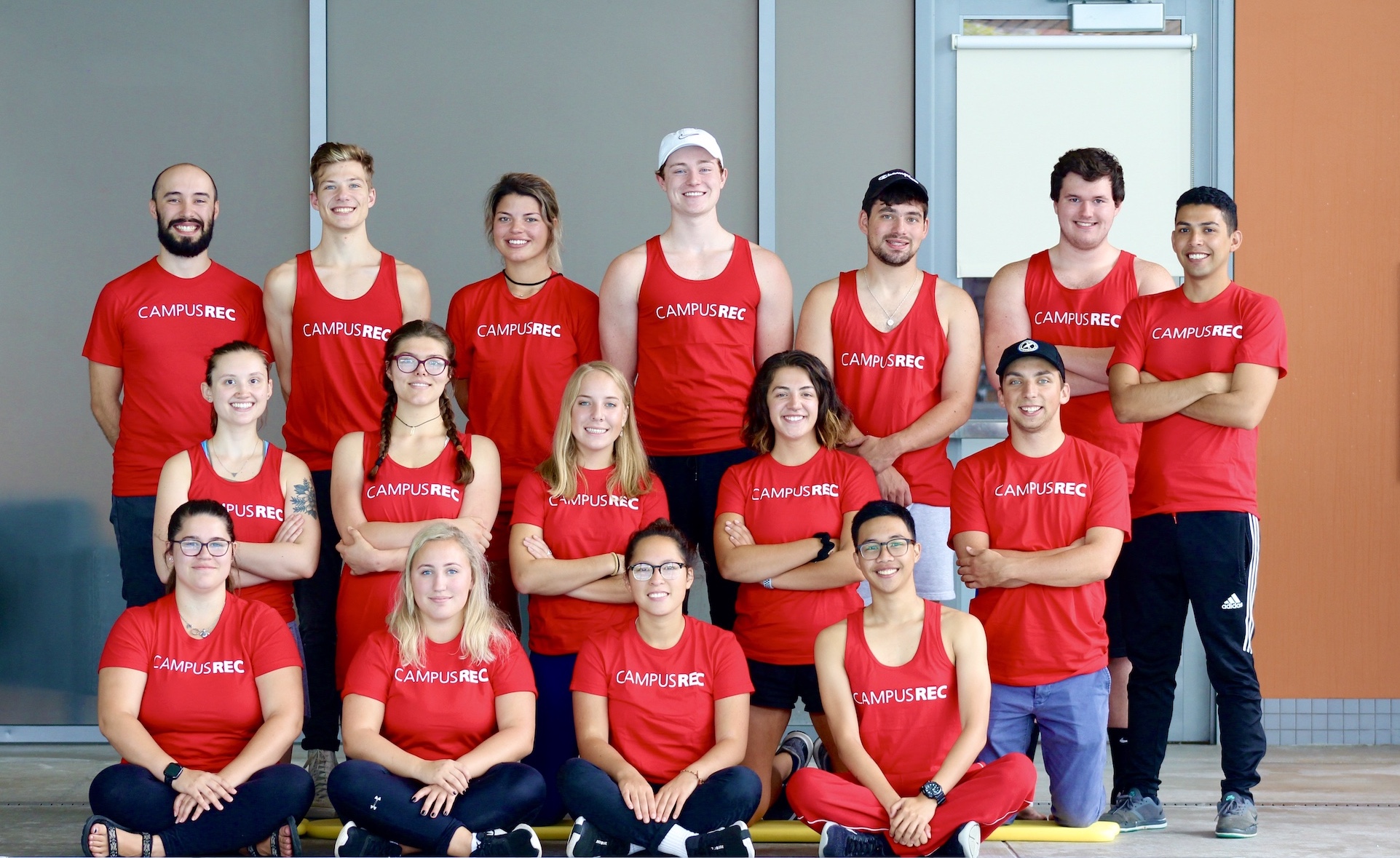 The Campus Rec Aquatics team poses all together in front of the Rec Center pool,  smiling and wearing their red Lifeguard shirts.