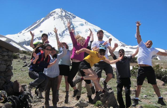 Group of students on an outdoor trip jumping in front of a snowy mountain. 