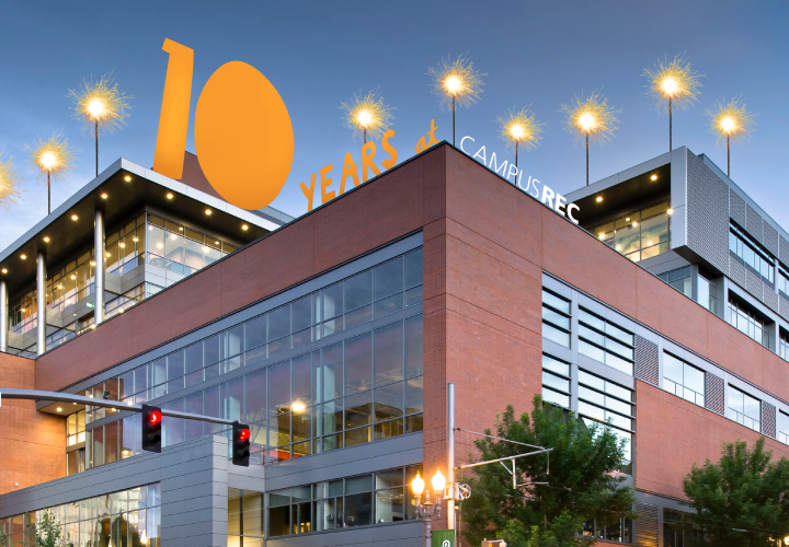 The Campus Recreation Center building at dusk with cars and buses driving by, with the words 10 years at Campus Rec.