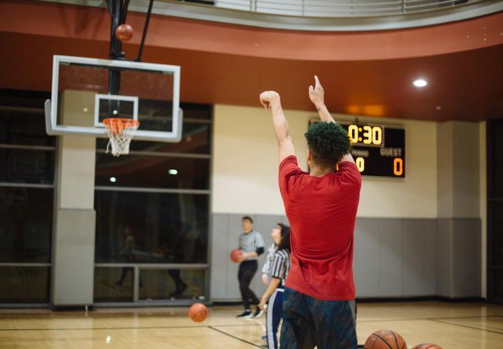 The image is of a person in a gym shooting a basketball into a net.