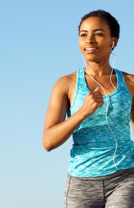 Person running outdoors with sun on their face and earbuds in their ears. The background is blue, like a clear blue sky.