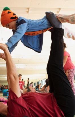 A parent holds their child up in a family-friendly yoga class