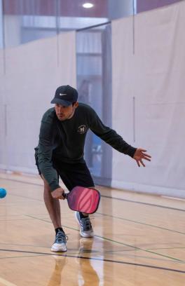 A person reach to hit a pickleball. 