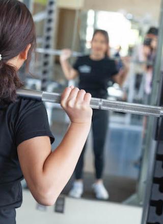 Personal Trainer standing in front of mirror doing squats with weights.