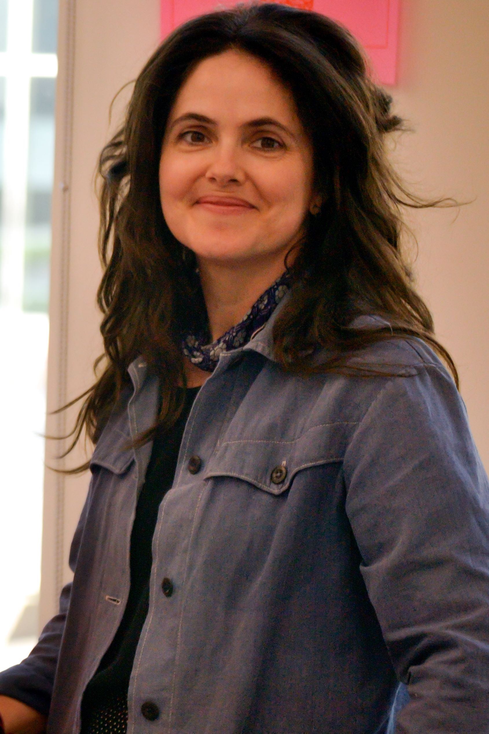 Alison Heryer stands with her left side closer to the camera, smiling and wearing a blue jacket