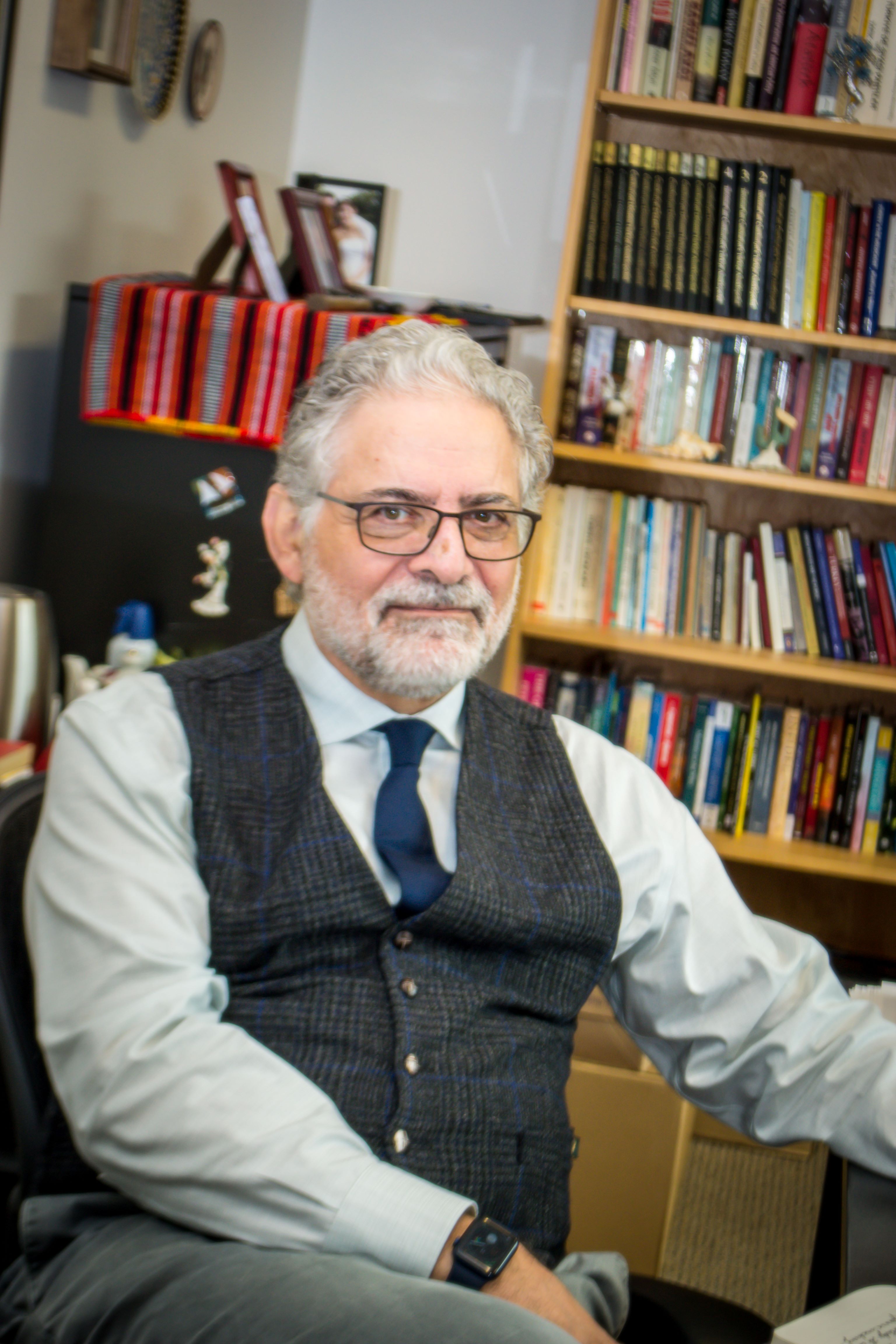 Birol Yesilada is seated, looking at the camera, with a bookcase behind him