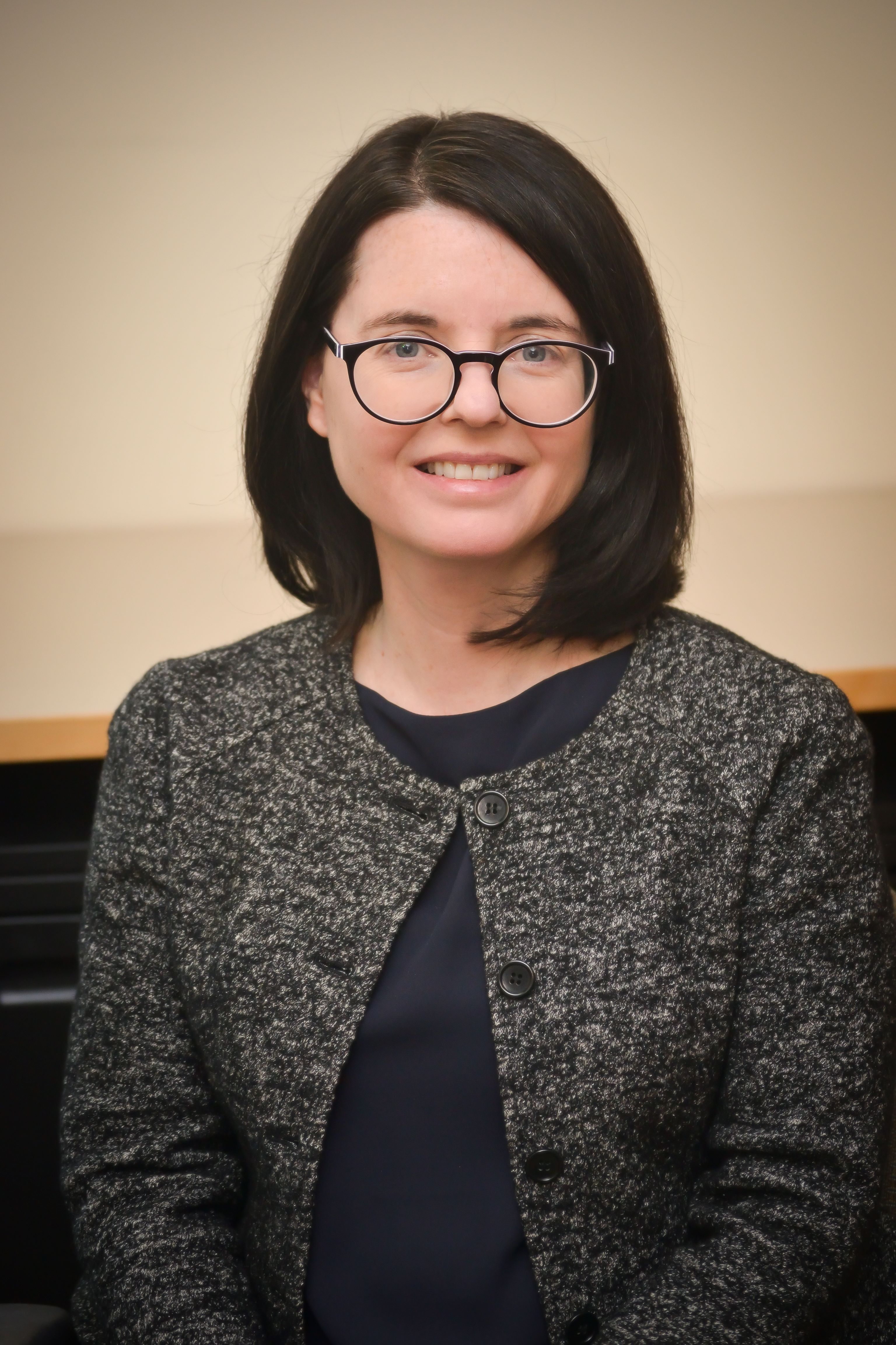 Lindsey Benstead faces the camera and smiles. She wears a gray jacket and dark-rimmed eyeglasses