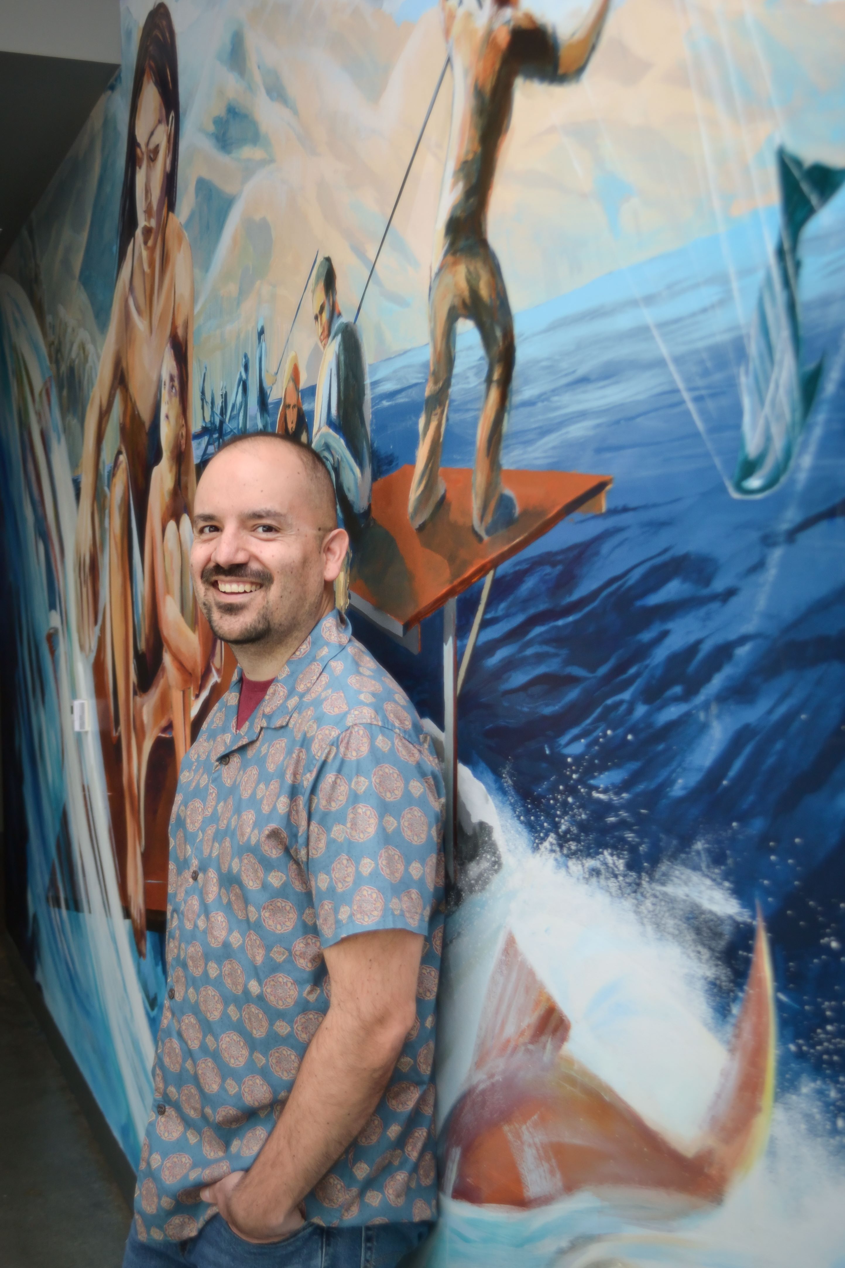 Town stands in front of a colorful mural with his left side turned to the camera, looking at the camera and smiling