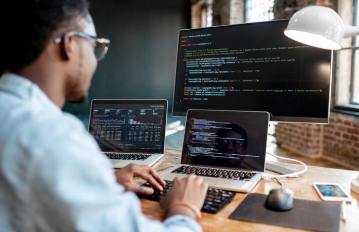 A person working with two laptops and a monitor.