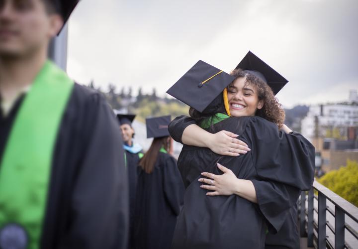 Graduates in cap and gown embrace after commencement ceremony