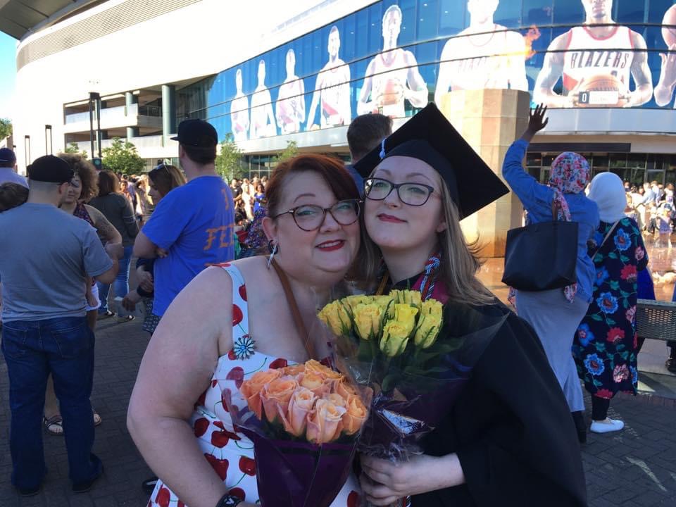 The image is of two people standing in front of a crowd, they are both holding flowers.