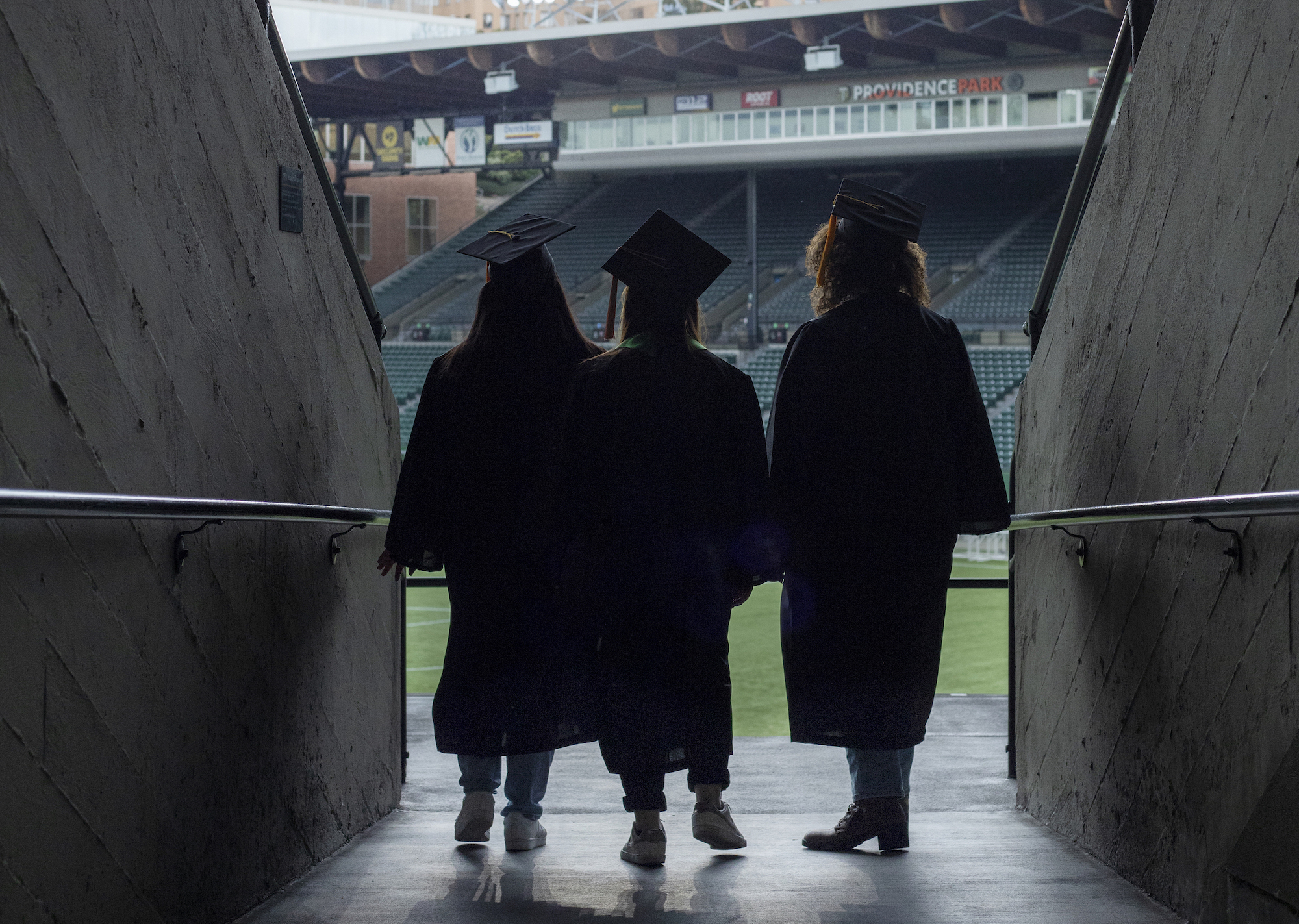 Three graduates look out into the Providence Park stadium