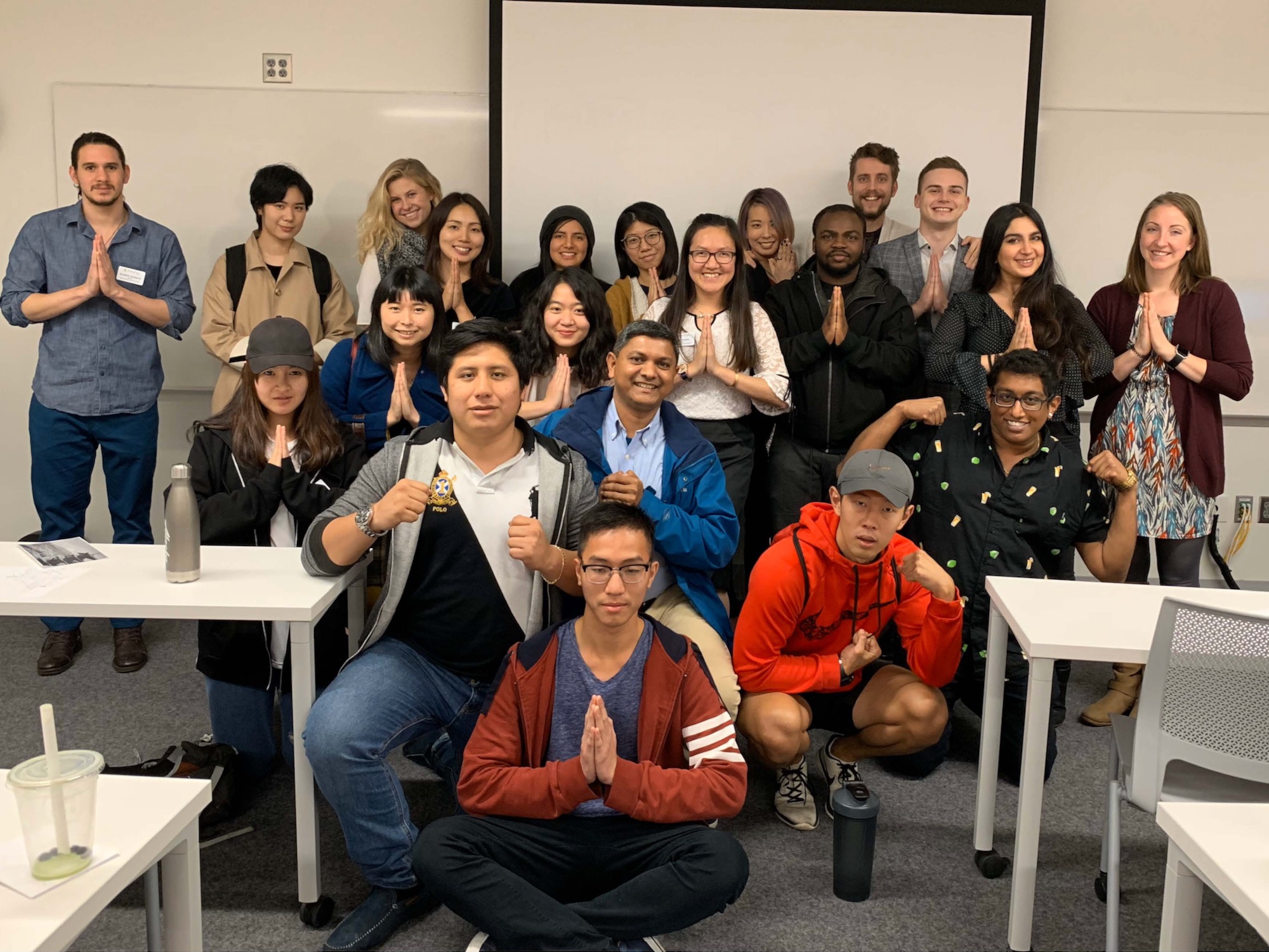 The image is of a group of people posing with their palms together.