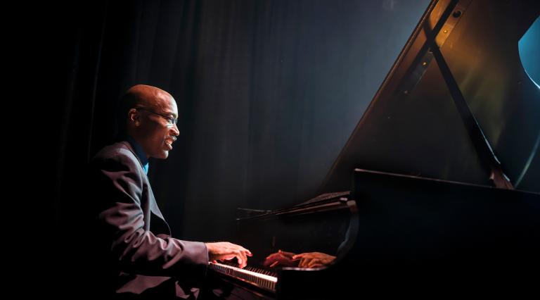 A PSU Music student playing the piano on a dark stage. 