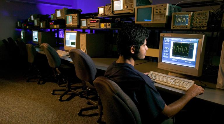 A PSU Technology Management student sitting in front of a computer in a dark computer lab.