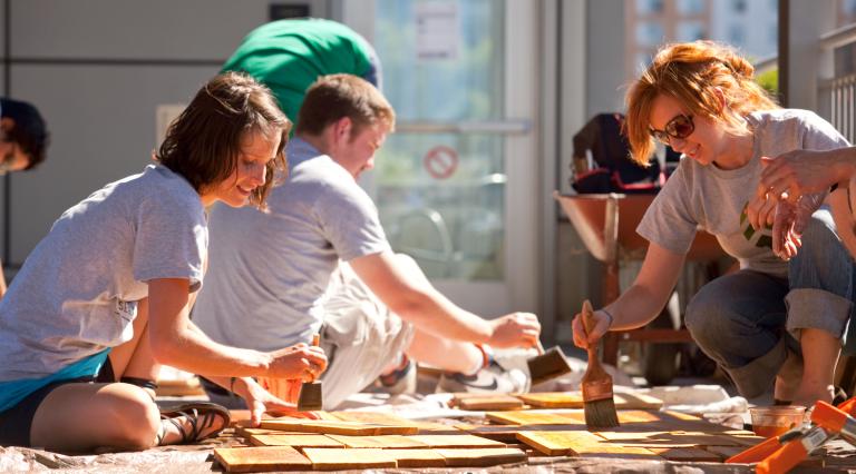 A group of PSU Community Development students painting on wood outside. 