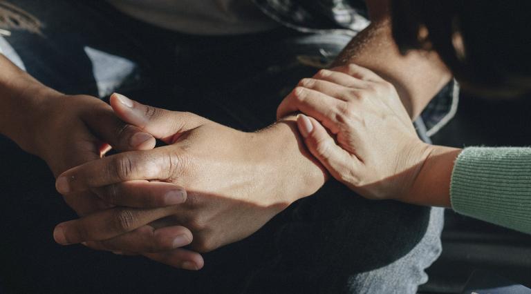 A hand rests on the forearm of a young man in comfort.