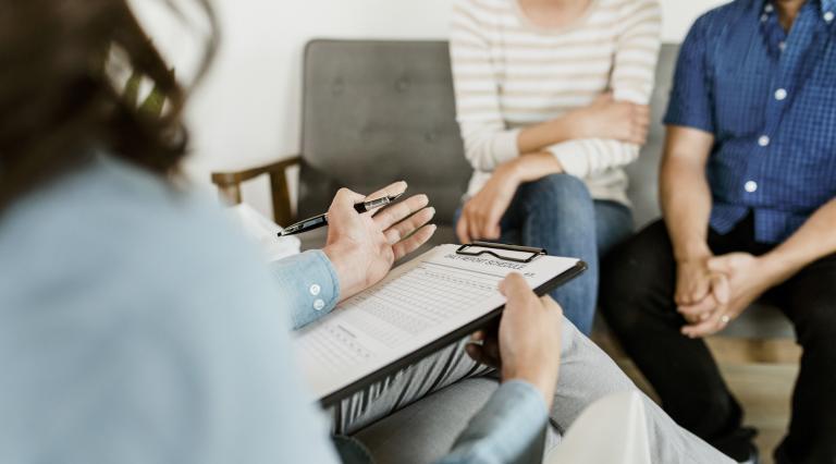 A therapist speaks with two individuals about their treatment schedule.