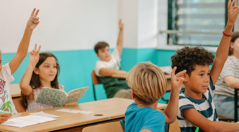 Students in an elementary classroom raising their hands.