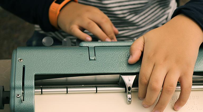 Close-up of a young boy's hands learning to use a Braille typewriter.