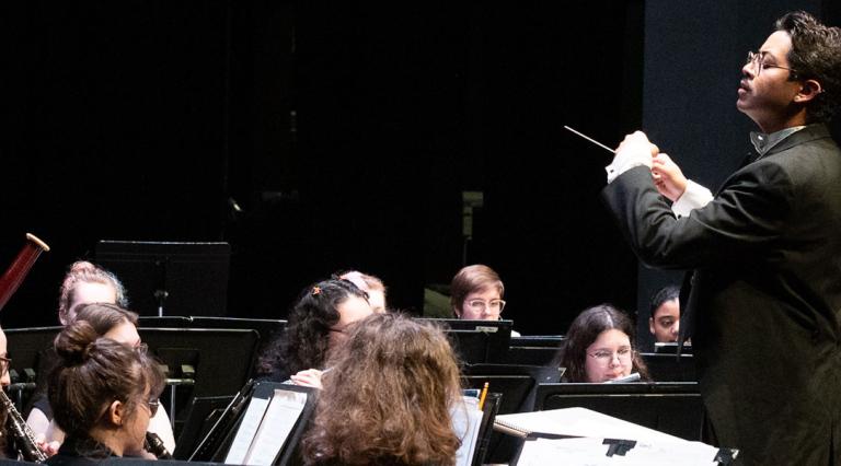 Students playing music in a practice room with a conductor