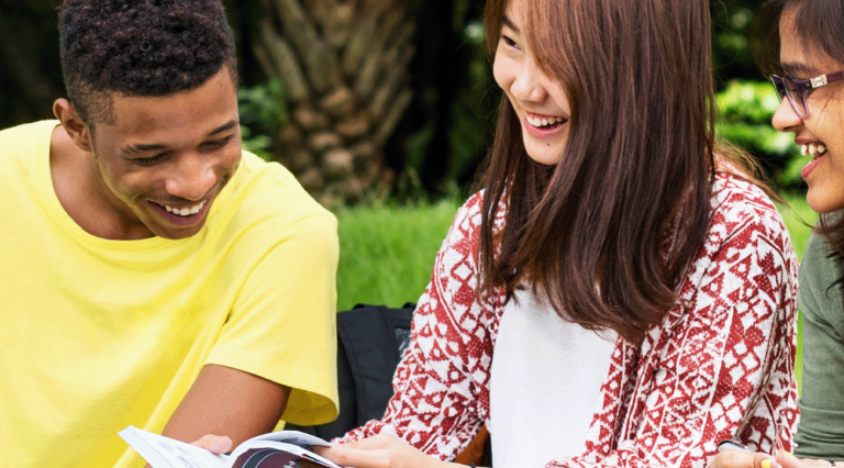 Three students sit in a park studying English together.