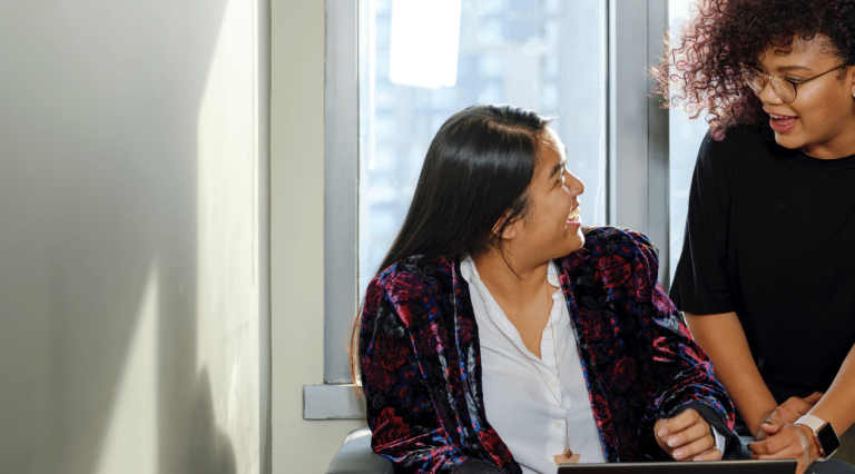 two graduate students working on a laptop and looking at each other while laughing