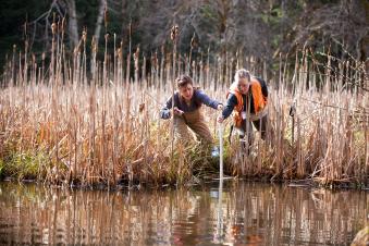 Two researchers taking a water sample in a bog